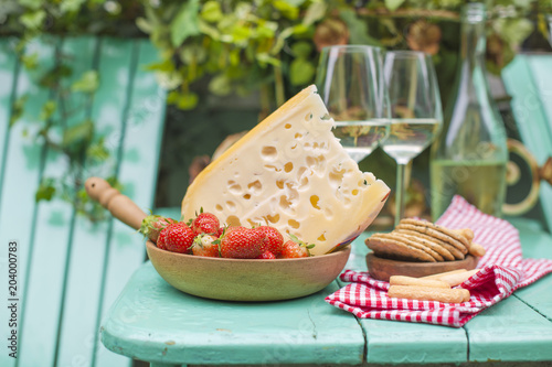 Dutch cheese with holes and strawberry. White wine in a glass and snacks. Food on the balcony