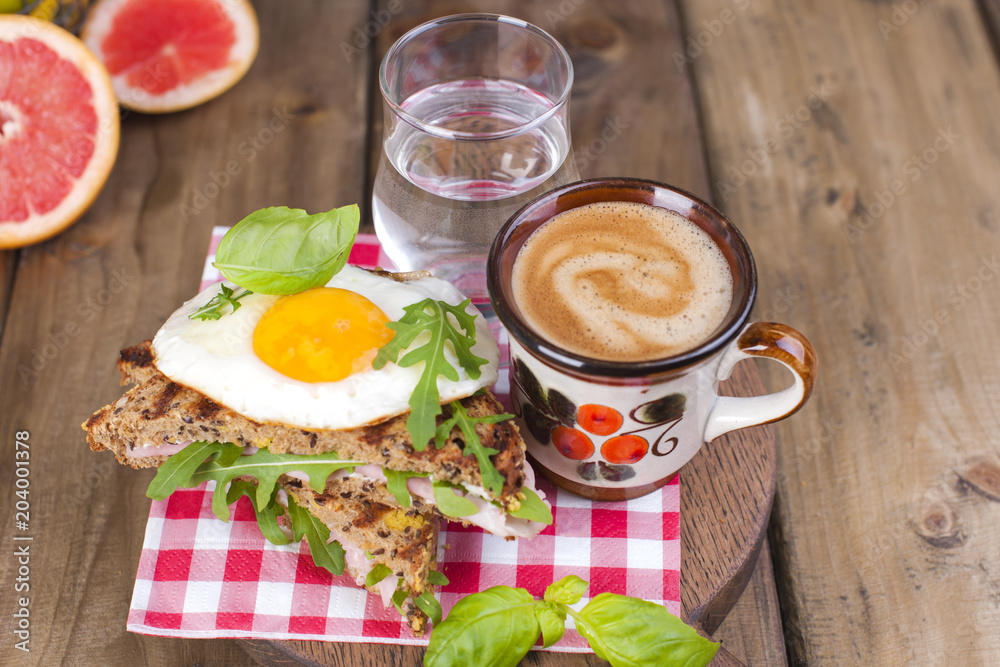 Toast with egg and bacon and basil. Coffee and a glass of water. Breakfast. Wooden background and Place for text. Lunch in the Netherlands. Toast with egg and bacon and basil. Coffee and a glass of water. Breakfast. Wooden background and Place for text. Lunch in the Netherlands.