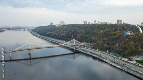 Aerial view of Bridge pedestrian across the Dnieper River, Embankment with traffic and the People's Friendship Arch on the mountain