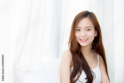 Portrait beautiful young asian woman standing and smile the window at bedroom while wake up with sunrise at morning, lifestyle and relax concept. © N_studio