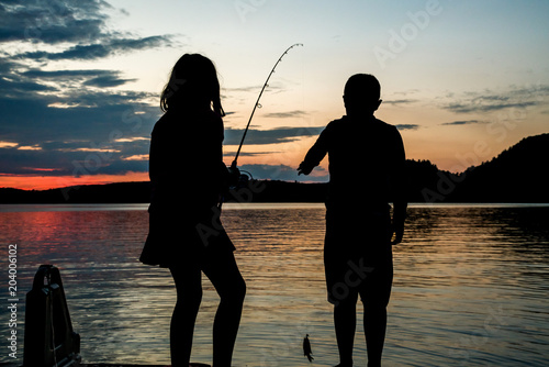 Children in silhouette, caught a small fish as sunsets across the lake