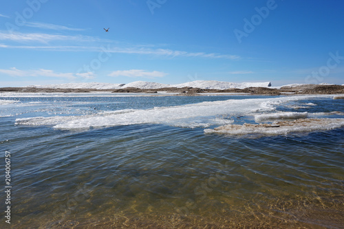 Lake shore on spring day with ice and snow in water, blue sky in the background