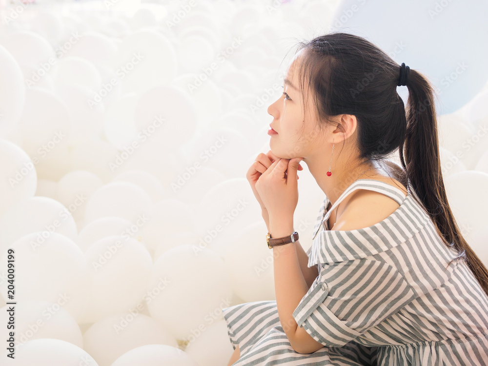 Portrait of beautiful Chinese girl in dress sit among white balloons with hands on chin, Beautiful Happy Young woman on birthday holiday party to make a wish. Portrait of beautiful Chinese girl in dress sit among white balloons with hands on chin, Beautiful Happy Young woman on birthday holiday party to make a wish.
