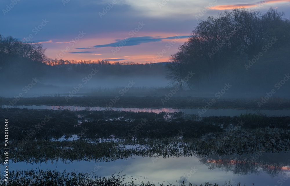 Peaceful foggy sunrise on the lake. The sunrise colors the sky in brilliant vivid colors