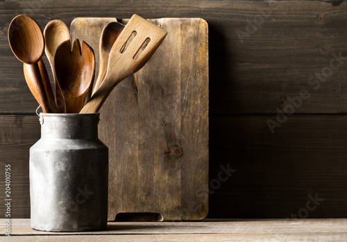 Wooden kitchen cooking tools with spoons and spatula with menu board in front of rustic wooden board background