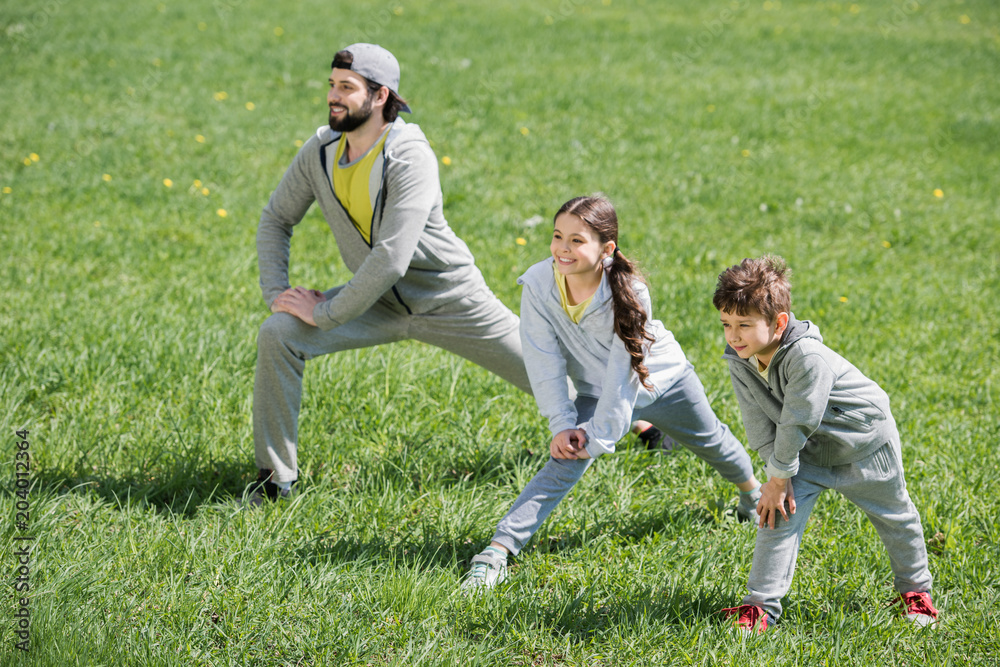 children and father doing physical exercise on meadow in park
