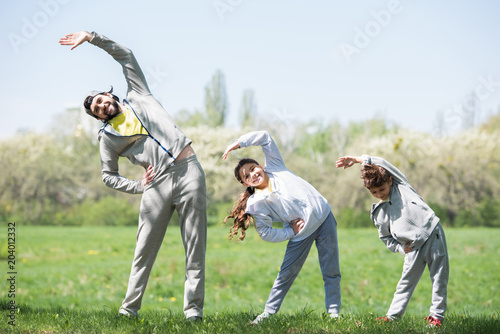 smiling father with daughter and son doing physical exercise on grassy meadow in park