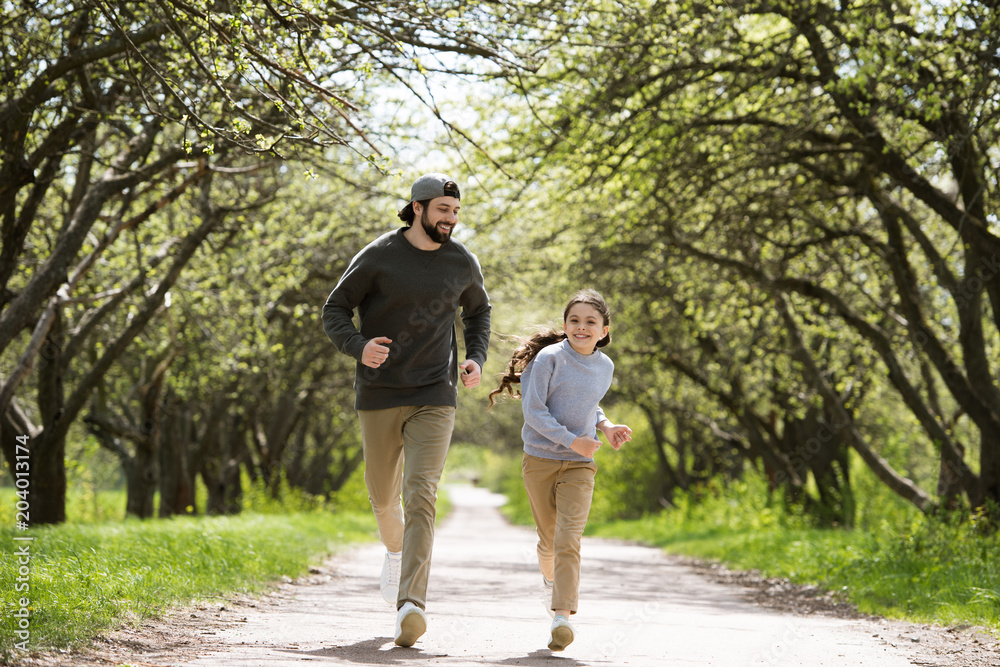 happy father and daughter running on path in park happy father and daughter running on path in park
