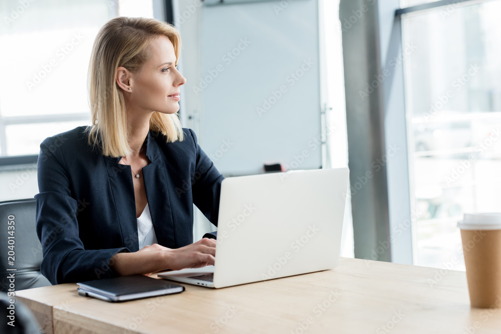 pensive buisnesswoman looking away while using laptop at workplace pensive buisnesswoman looking away while using laptop at workplace