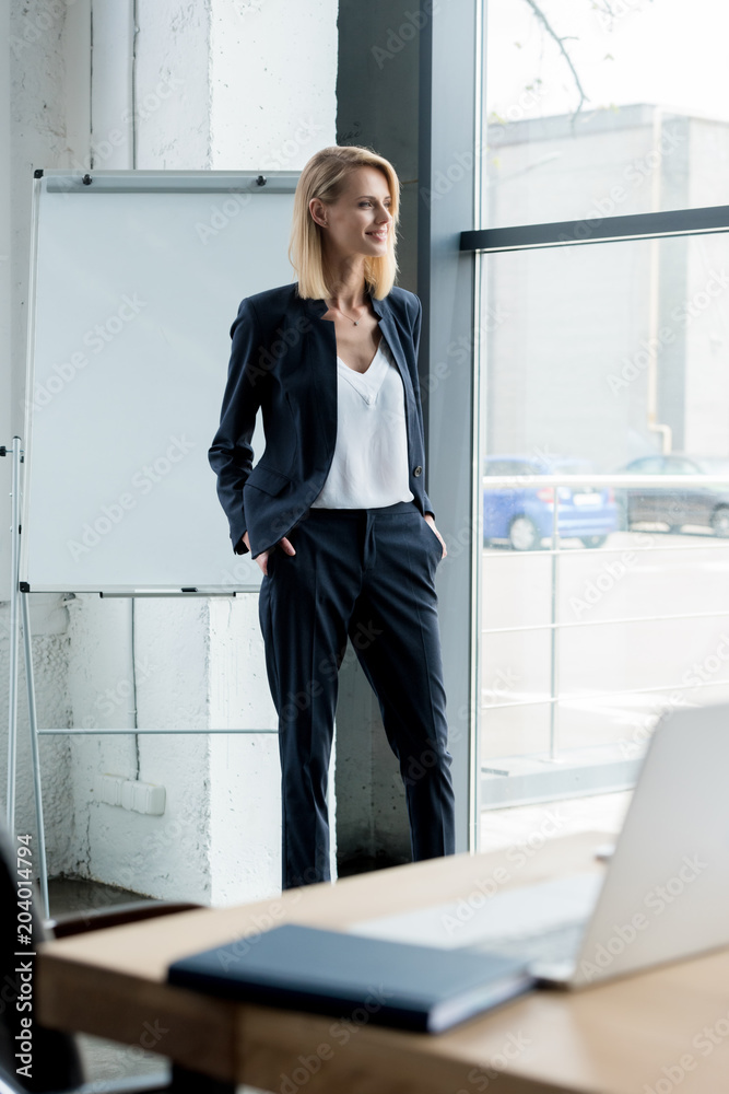 stylish blonde businesswoman standing with hands in pockets and looking at window stylish blonde businesswoman standing with hands in pockets and looking at window