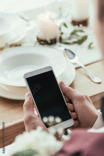 cropped shot of groom using smartphone at served rustic table