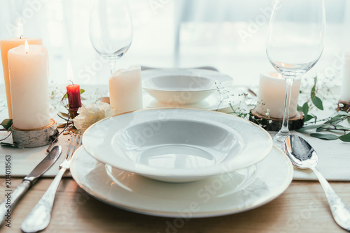close up view of stylish table setting with candles, empty wineglasses and plates for rustic wedding