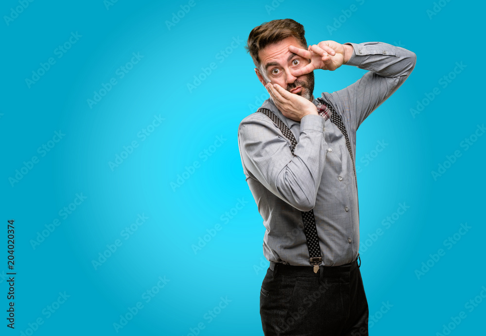 Middle age man, with beard and bow tie looking at camera through fingers in victory gesture winking the eye and blowing a kiss Middle age man, with beard and bow tie looking at camera through fingers in victory gesture winking the eye and blowing a kiss
