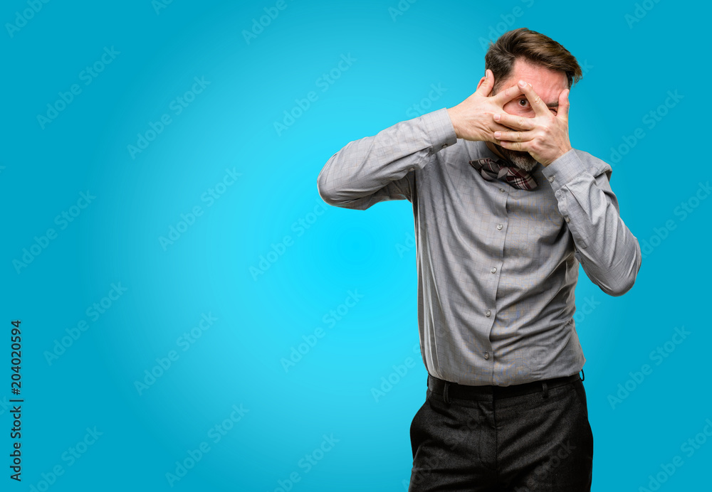 Middle age man, with beard and bow tie smiling having shy look peeking through fingers, covering face with hands looking confusedly broadly Middle age man, with beard and bow tie smiling having shy look peeking through fingers, covering face with hands looking confusedly broadly