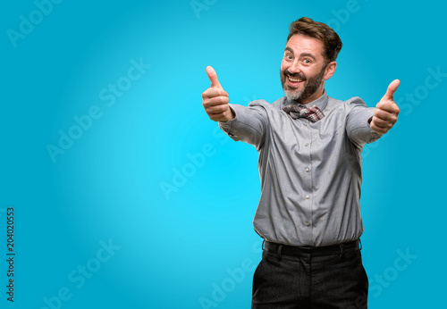 Middle age man, with beard and bow tie stand happy and positive with thumbs up approving with a big smile expressing okay gesture