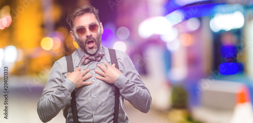 Middle age man, with beard and bow tie happy and surprised cheering expressing wow gesture at night club