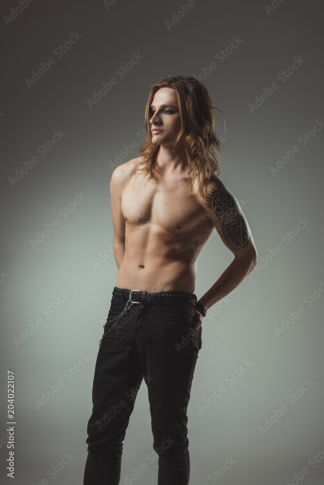 shirtless man with long hair and tattoo posing in black jeans, isolated on grey shirtless man with long hair and tattoo posing in black jeans, isolated on grey