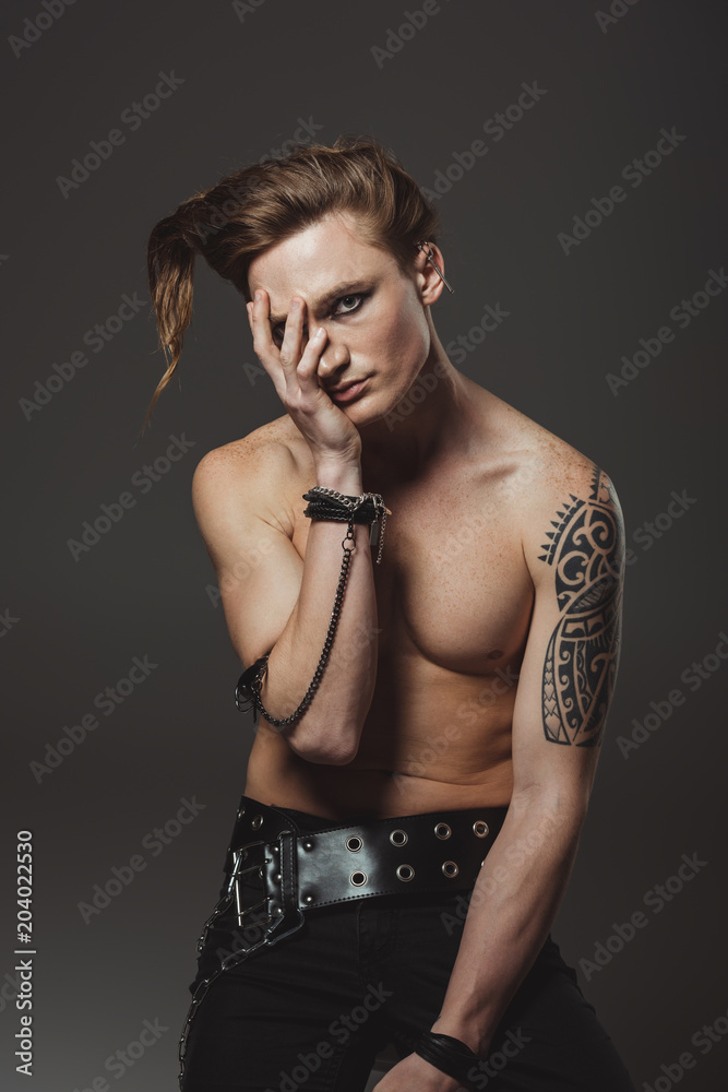 handsome shirtless man with tattoo on hand and strange hairstyle, isolated on grey