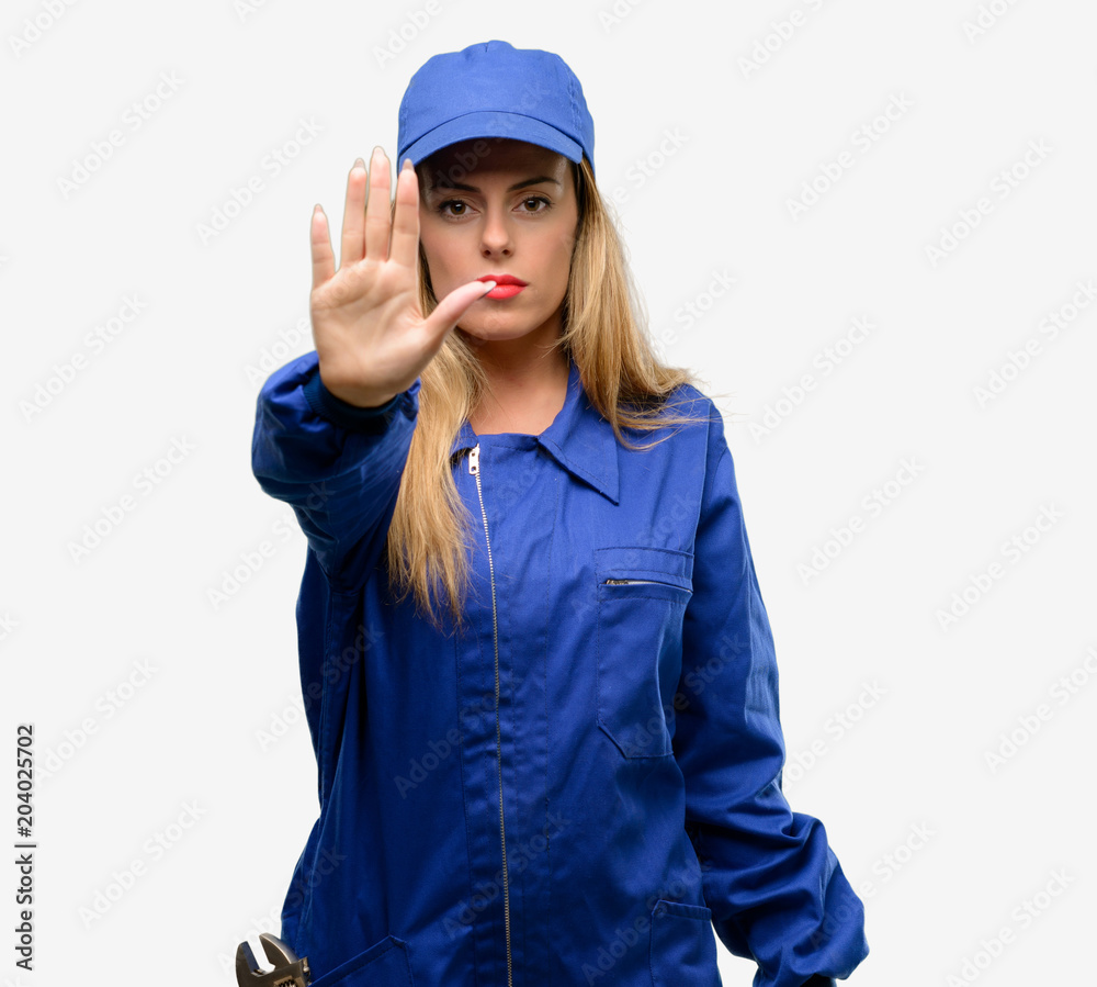 Young plumber woman annoyed with bad attitude making stop sign with hand, saying no, expressing security, defense or restriction, maybe pushing Young plumber woman annoyed with bad attitude making stop sign with hand, saying no, expressing security, defense or restriction, maybe pushing