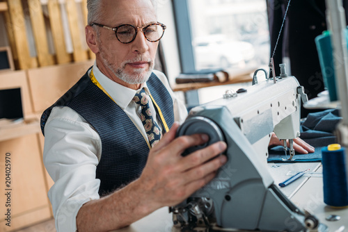 handsome tailor sewing cloth with sewing machine at sewing workshop