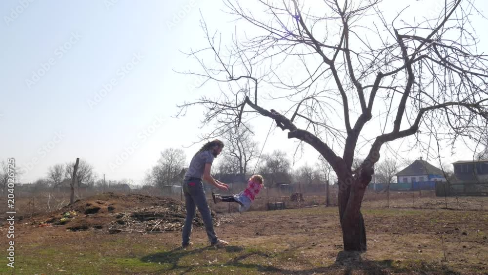 Father pushing his daughter on the swing while having fun in the park Father pushing his daughter on the swing while having fun in the park