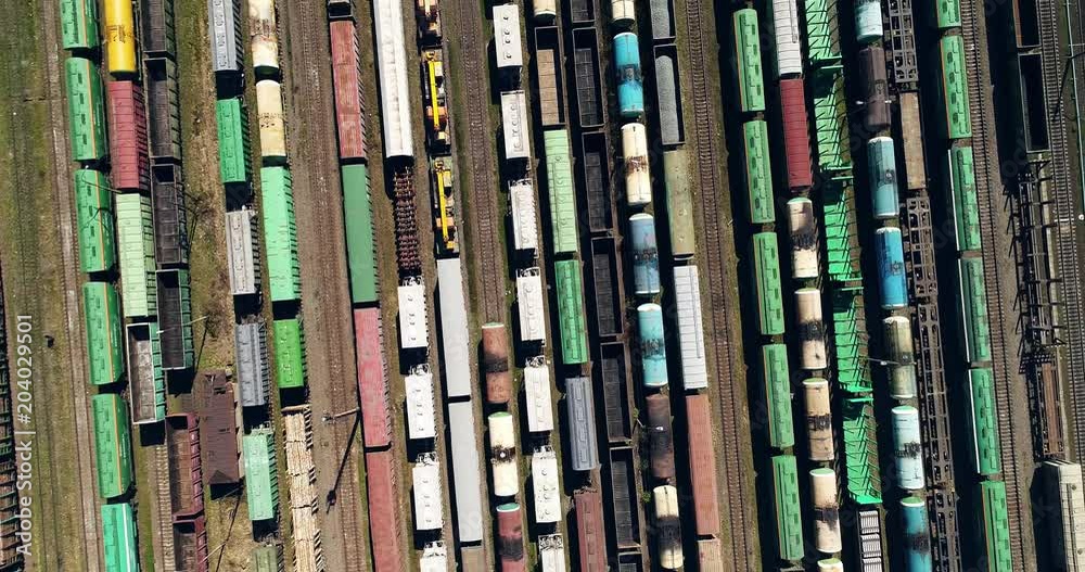 AERIAL. Camera moving out. Cargo trains close-up. Aerial view of colorful freight trains on the railway station. Wagons with goods on railroad. Heavy industry.