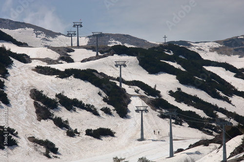Widok trasy narciarskiej i wyciągu w górach po sezonie zimowym, resztki śniegu opnieją, widać ziemię, roślinność, pusto