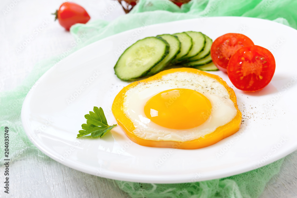 Fried egg in a circle of sweet pepper on a white plate with fresh vegetables on a white wooden background. Delicious healthy breakfast. Proper nutrition. Fried egg in a circle of sweet pepper on a white plate with fresh vegetables on a white wooden background. Delicious healthy breakfast. Proper nutrition.
