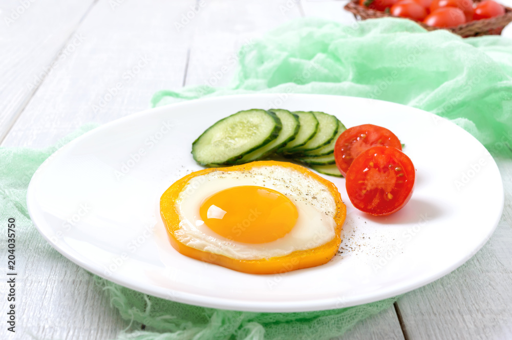 Fried egg in a circle of sweet pepper on a white plate with fresh vegetables on a white wooden background. Delicious healthy breakfast. Proper nutrition. Fried egg in a circle of sweet pepper on a white plate with fresh vegetables on a white wooden background. Delicious healthy breakfast. Proper nutrition.