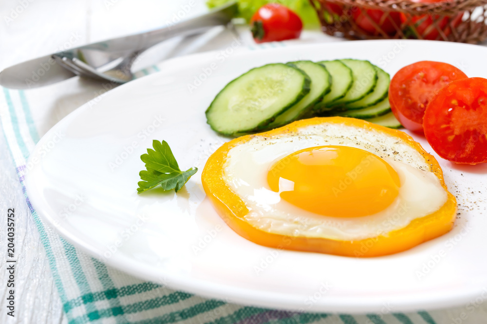 Fried egg in a circle of sweet pepper on a white plate with fresh vegetables on a white wooden background. Delicious healthy breakfast. Proper nutrition. Fried egg in a circle of sweet pepper on a white plate with fresh vegetables on a white wooden background. Delicious healthy breakfast. Proper nutrition.