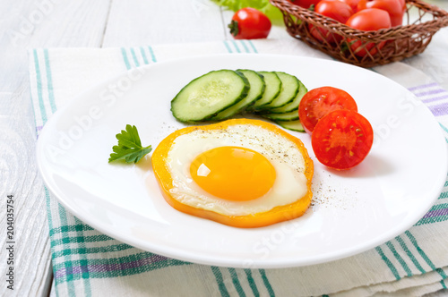 Fried egg in a circle of sweet pepper on a white plate with fresh vegetables on a white wooden background. Delicious healthy breakfast. Proper nutrition.