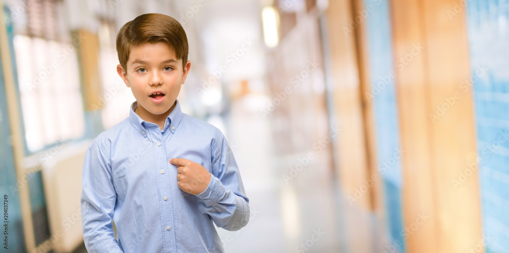 Handsome toddler child with green eyes happy and surprised cheering expressing wow gesture, pointing with finger at school corridor Handsome toddler child with green eyes happy and surprised cheering expressing wow gesture, pointing with finger at school corridor