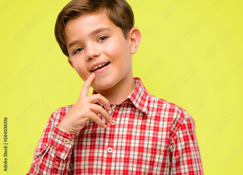 Handsome toddler child with green eyes confident and happy with a big natural smile laughing over yellow background Handsome toddler child with green eyes confident and happy with a big natural smile laughing over yellow background