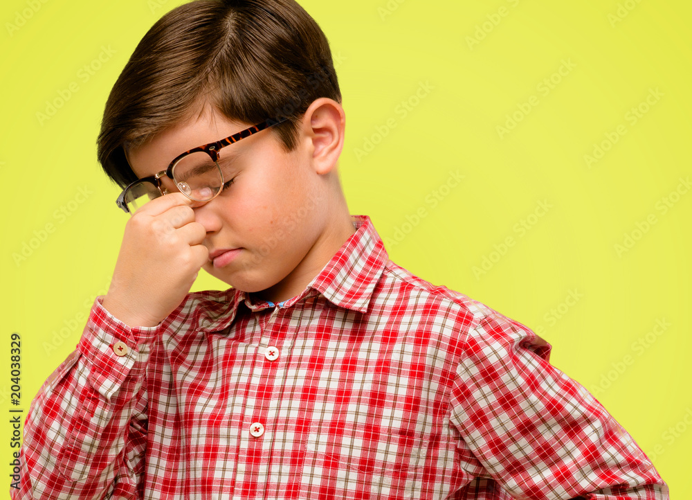 Handsome toddler child with green eyes with sleepy expression, being overworked and tired, rubbes nose because of weariness over yellow background Handsome toddler child with green eyes with sleepy expression, being overworked and tired, rubbes nose because of weariness over yellow background