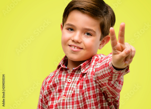 Handsome toddler child with green eyes raising fingers, number two over yellow background
