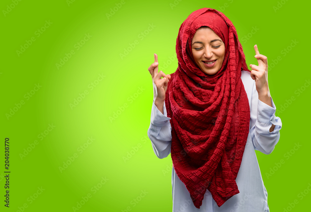 Young arab woman wearing hijab with crossed fingers asking for good luck Young arab woman wearing hijab with crossed fingers asking for good luck