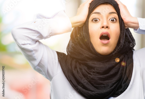 Young arab woman wearing hijab stressful keeping hands on head, terrified in panic, shouting