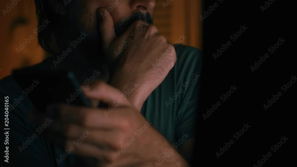 Bored man wasting time using mobile phone in dark room interior, low key Bored man wasting time using mobile phone in dark room interior, low key