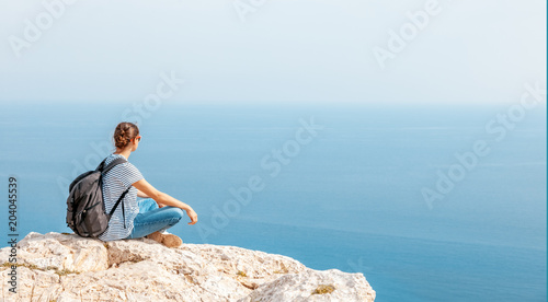 A girl traveler sits on a rock and admires the blue boundless sea  freedom  travel  unity with nature
