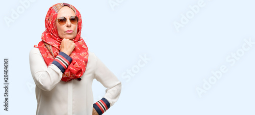 Middle age muslim arab woman wearing hijab thinking and looking up expressing doubt and wonder isolated blue background © Krakenimages.com