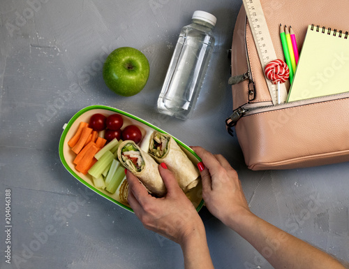 Female hands packing dinner in lunchbox on grey table