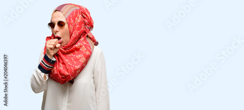Middle age muslim arab woman wearing hijab sick and coughing, suffering asthma or bronchitis, medicine concept isolated blue background