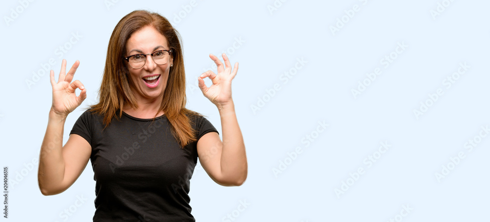 Middle age woman wearing black shirt and glasses doing ok sign gesture with both hands expressing meditation and relaxation isolated blue background Middle age woman wearing black shirt and glasses doing ok sign gesture with both hands expressing meditation and relaxation isolated blue background