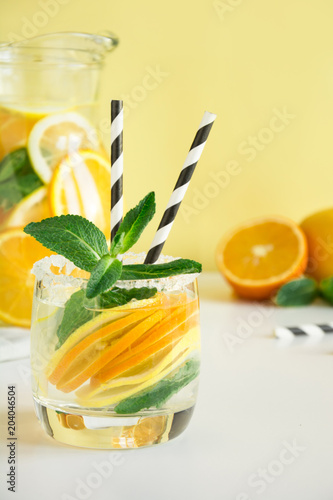 Fruits water with lemon, orange and mint on yellow background.