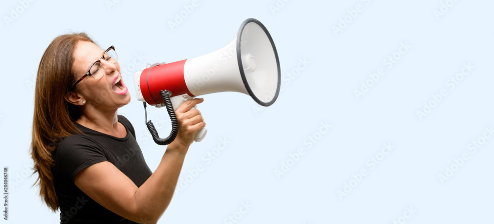 Middle age woman wearing black shirt and glasses communicates shouting loud holding a megaphone, expressing success and positive concept, idea for marketing or sales isolated blue background Middle age woman wearing black shirt and glasses communicates shouting loud holding a megaphone, expressing success and positive concept, idea for marketing or sales isolated blue background
