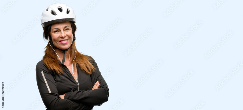 Obraz premium Middle age cyclist woman using earphones with crossed arms confident and happy with a big natural smile laughing isolated blue background