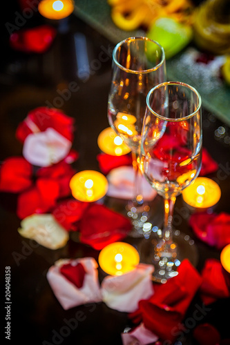 close-up two glasses for champagne, candles and rose petals