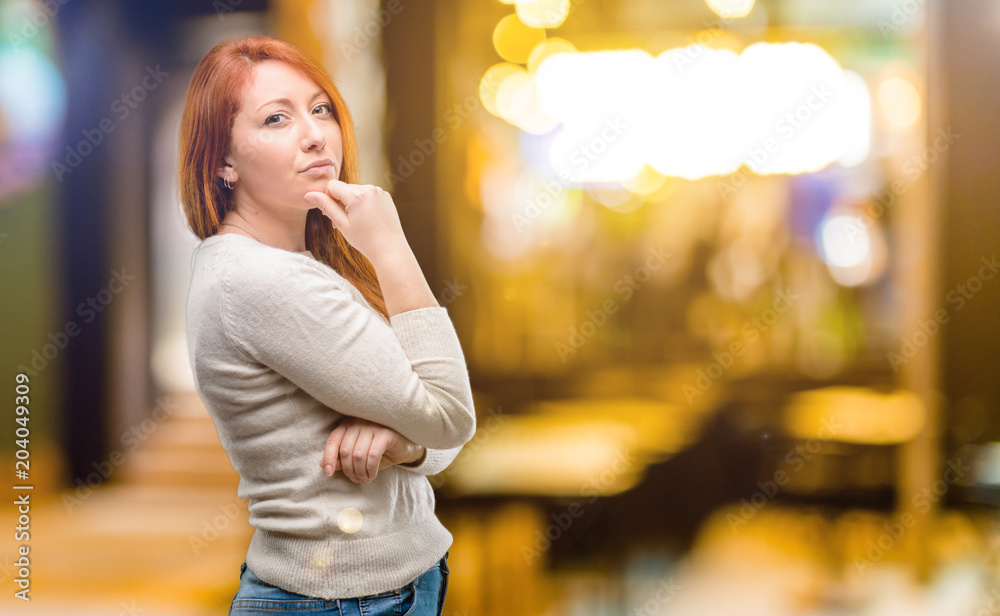 Beautiful young redhead woman thinking thoughtful with smart face at night