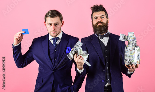 Bank account concept. Men in suit, businessmen with jar full of cash and credit card, pink background. Mature man wants to put money into bank account, get credit card, electronic money. photo