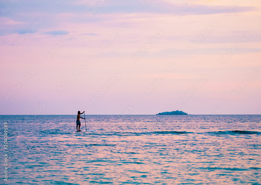 standup paddler auf dem Meer in der Dämmerung mit einer kleinen Insel